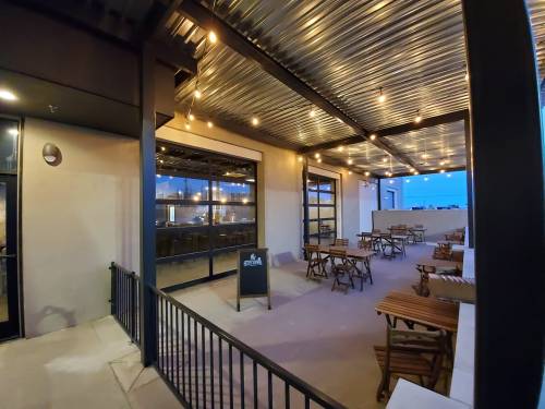 Outdoor seating area of a restaurant with wooden tables, string lights, and a view of the evening sky.