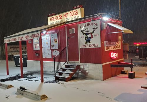 A red food stand named "Firehouse Hot Dogs" with a snowy backdrop, featuring a menu and an "Open" sign.