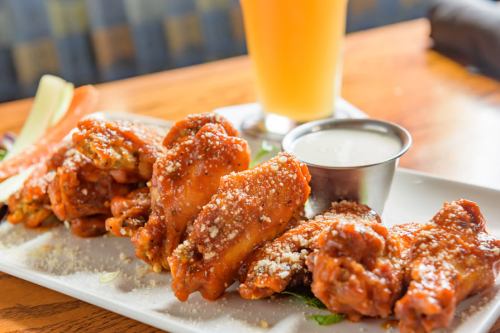 A plate of spicy chicken wings topped with cheese, served with a side of ranch dressing and a glass of beer.