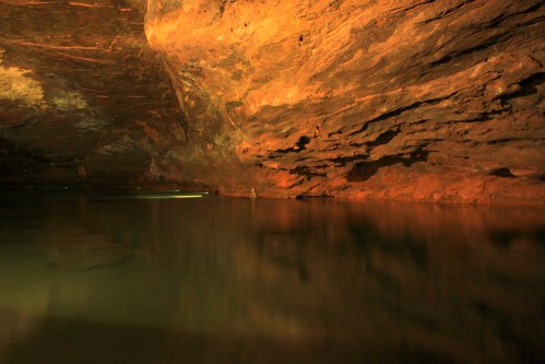 A serene underground cave with a calm water surface reflecting the rocky, illuminated ceiling.