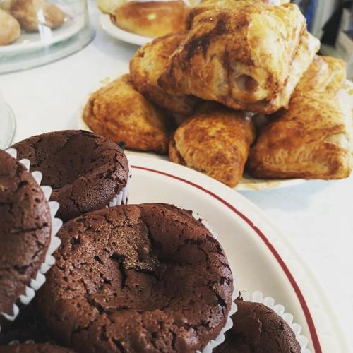 A plate of chocolate muffins in the foreground, with a stack of golden-brown pastries in the background.