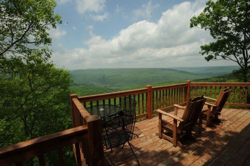 A wooden deck with chairs overlooks a lush green valley under a partly cloudy sky.