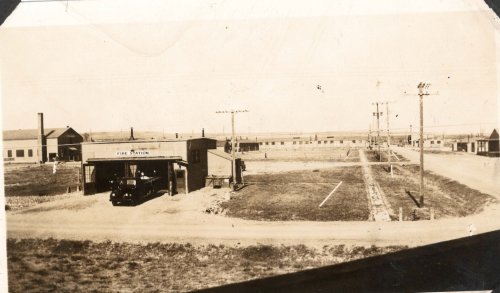 Historic black-and-white photo of a fire station with surrounding buildings and open land in a rural setting.