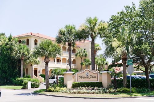 A sunny view of a Mediterranean-style building surrounded by palm trees and greenery, with a sign reading "Kings and Prince."