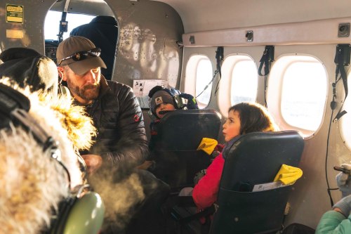 A man and two children sit inside a small plane, with sunlight streaming through the windows.