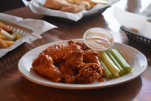 A plate of crispy chicken wings with celery sticks and a small cup of dipping sauce on a table.
