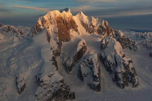 Aerial view of a majestic snow-capped mountain range under soft, golden light.