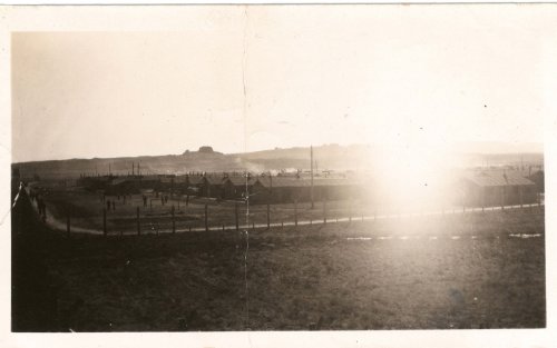 Black and white photo of a rural settlement with buildings and a distant landscape, illuminated by sunlight.
