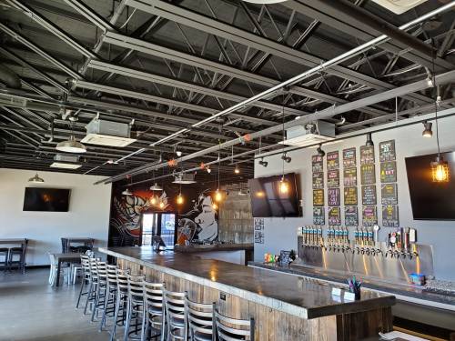 Interior of a modern bar with a long wooden counter, multiple beer taps, and a stylish industrial design.