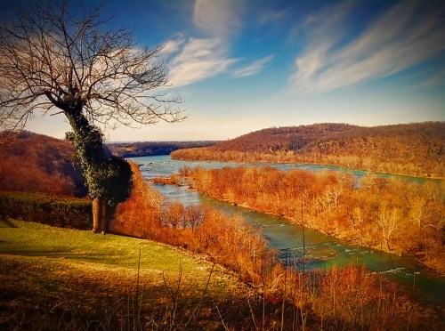 A scenic view of a river winding through autumn trees under a blue sky with wispy clouds.