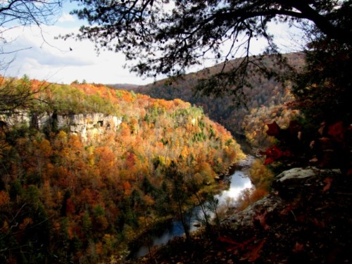A scenic view of a river winding through a valley surrounded by vibrant autumn foliage and rocky cliffs.