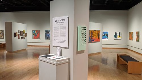Art gallery interior featuring various abstract paintings on the walls, with a display sign for an exhibition titled "Abstraction."
