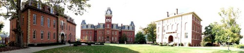Panoramic view of a historic campus featuring brick buildings and a green lawn under a clear sky.