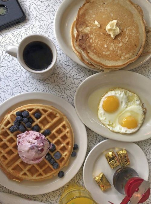 A breakfast spread featuring pancakes, a waffle with ice cream and blueberries, fried eggs, coffee, and syrup.