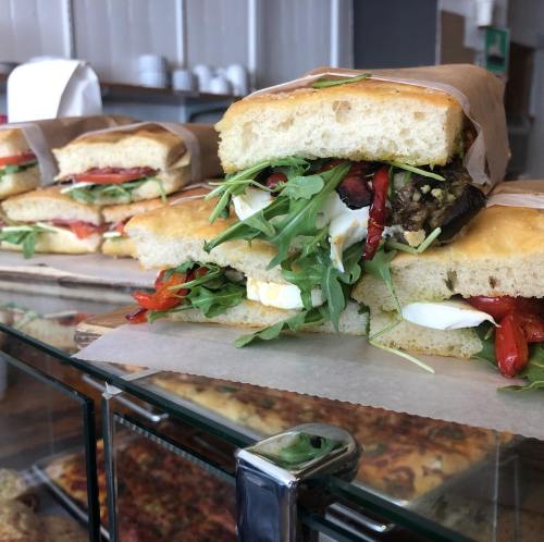 A close-up of a sandwich filled with roasted peppers, greens, and creamy cheese, displayed in a glass case.