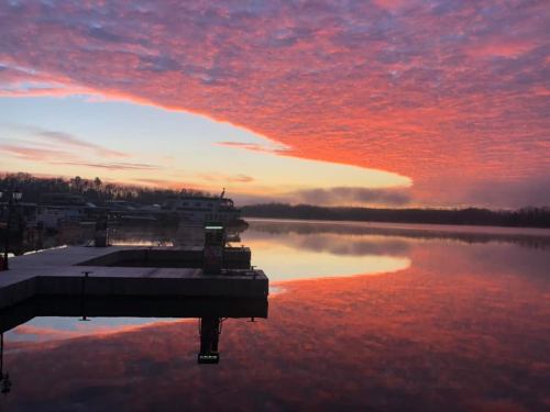 A serene lake at sunset, reflecting vibrant pink and orange clouds, with a dock and boats in the background.