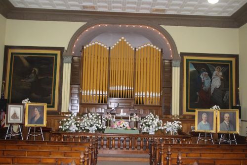Interior of a church featuring an organ, floral arrangements, and framed portraits on display.