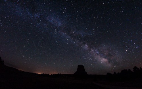 A starry night sky with the Milky Way visible above a silhouette of a mountain or rock formation.