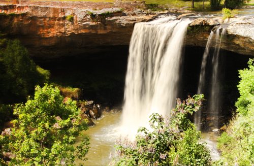 A waterfall cascading over a rocky ledge, surrounded by lush greenery and a serene pool below.