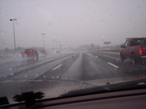 A view of a wet highway during heavy rain, with vehicles driving in the distance and low visibility.