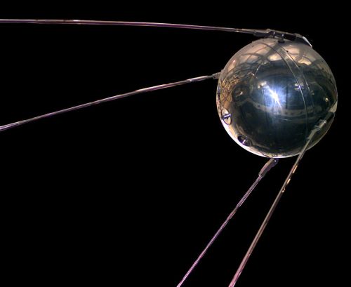 A shiny metallic sphere with antennas, representing the Sputnik satellite against a black background.