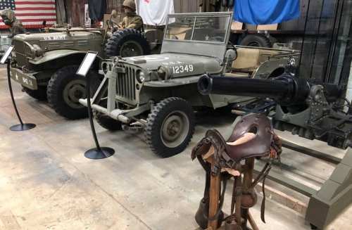 Two vintage military vehicles displayed in a museum, with a saddle and historical artifacts in the foreground.