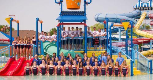 A large group of people in swimsuits poses in front of colorful water slides and a play structure at a water park.