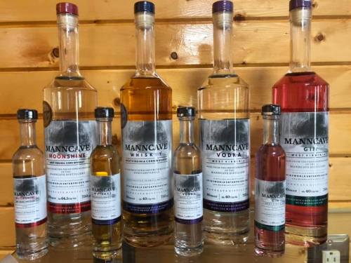 A display of various bottles of MannCave spirits, including whiskey, vodka, gin, and moonshine, on a wooden shelf.