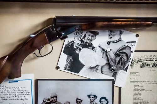 A vintage shotgun displayed on a wall, accompanied by black-and-white photos and documents related to hunting.