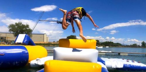A person in swimwear jumps off an inflatable structure into a lake on a sunny day.