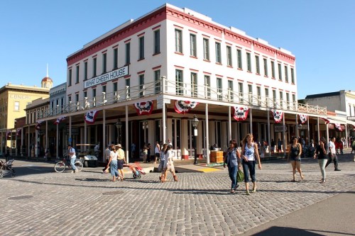 Historic building with a sign reading "Mary Cheever House," bustling street with people and festive decorations.