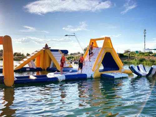 A colorful inflatable water park with slides and climbing structures, people in life jackets enjoying the water.