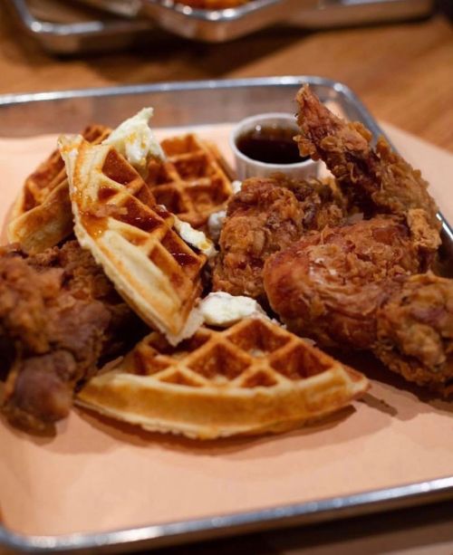 A plate of crispy fried chicken served with golden waffles and a small cup of syrup.
