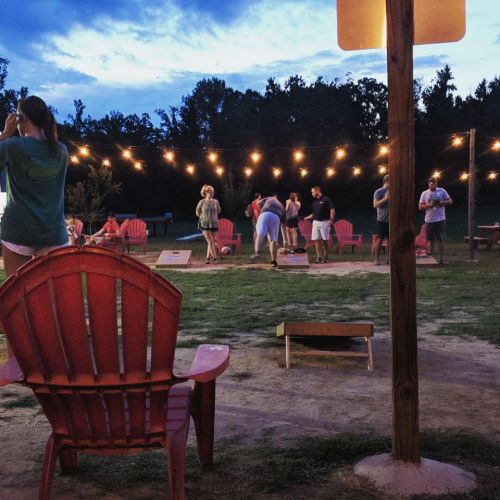 A lively outdoor gathering at dusk with people playing games and string lights illuminating the scene.