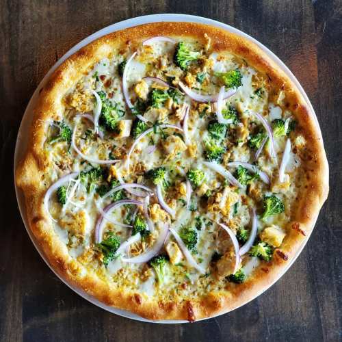 A round pizza topped with chicken, broccoli, red onions, and a creamy sauce on a golden crust.