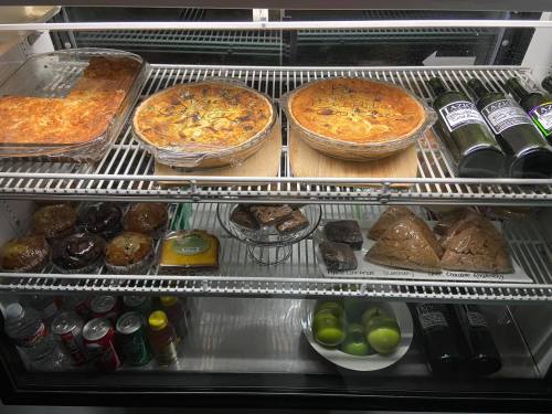 A display case with lasagna, quiches, drinks, baked goods, and fresh limes.