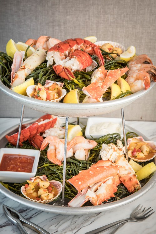 A two-tier seafood platter featuring lobster, shrimp, crab, and lemon wedges on a bed of seaweed.
