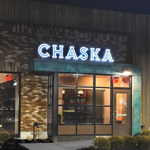 Exterior of a restaurant named "Chaska" with illuminated signage at night, featuring a modern design and large windows.