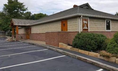 A single-story building with a textured exterior, wooden doors, and a landscaped parking area.