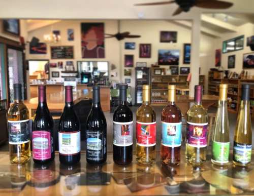 A display of various wine bottles on a counter in a cozy tasting room with artwork on the walls.