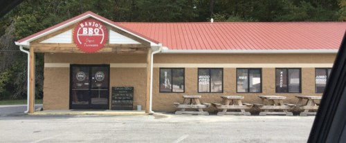 Exterior of Banjo's BBQ in Dayton, Tennessee, featuring a red roof, picnic tables, and large windows with menu items.