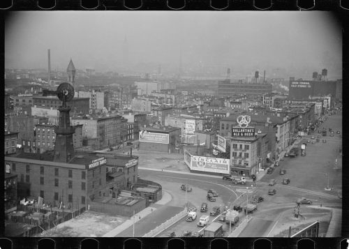 Aerial view of a cityscape with buildings, vintage cars, and advertisements, shrouded in a hazy atmosphere.