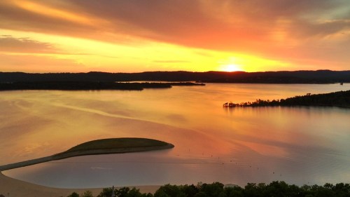 A serene sunset over a calm lake, with vibrant orange and yellow hues reflecting on the water's surface.
