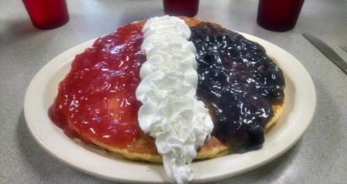 A large pancake topped with whipped cream and divided into three sections of strawberry, blueberry, and raspberry sauces.