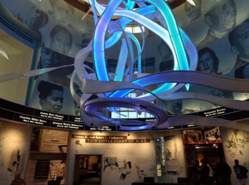 A modern museum interior featuring a colorful light installation and historical portraits on the walls.