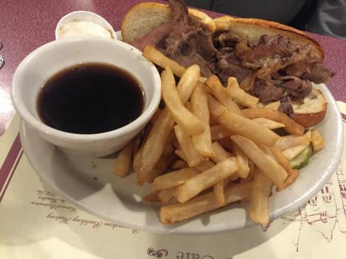 A plate with a sandwich filled with roast beef, a side of fries, and a small bowl of dipping sauce.