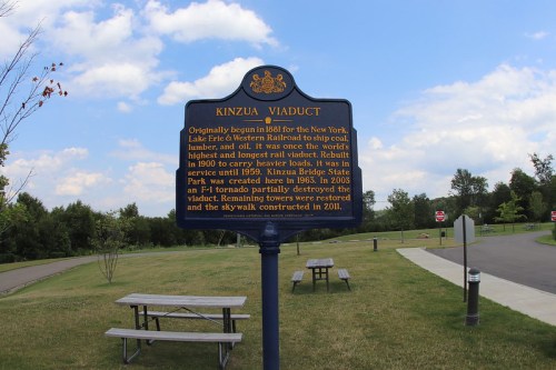 Sign about the Kinzua Viaduct's history, with a park and blue sky in the background. Tables are visible in the foreground.