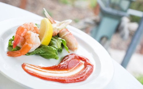 A plate with shrimp, lemon, lettuce, and a decorative swirl of ketchup.