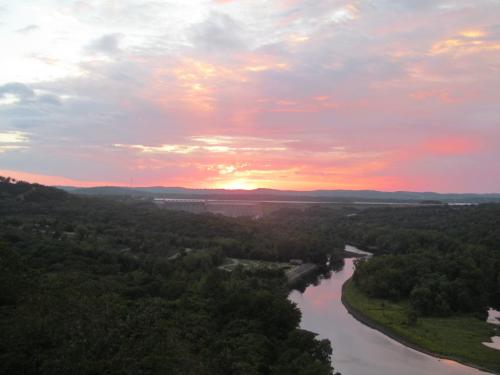 A vibrant sunset over a river, with lush green hills and a colorful sky filled with pink and orange hues.
