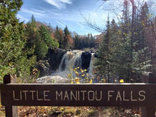 A scenic view of Little Manitou Falls surrounded by trees and autumn foliage under a clear blue sky.